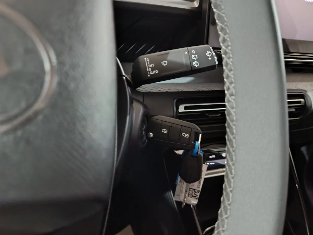 Vue rapprochée du volant cuir et de la clé insérée sur une Citroën C3 hybride noire, avec commandes au volant visibles.