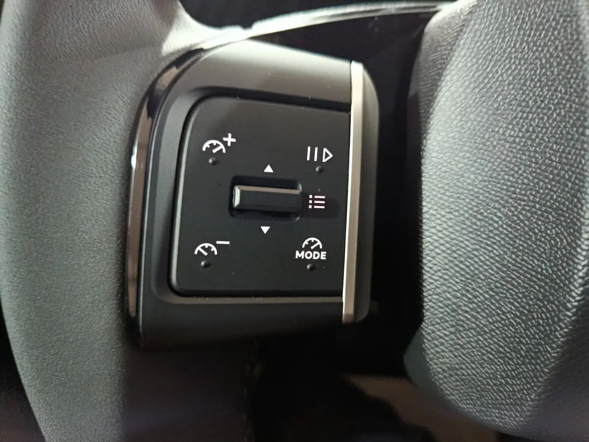 Gros plan sur les commandes de régulateur de vitesse sur le volant cuir noir de la Citroën C3 hybride 2025.