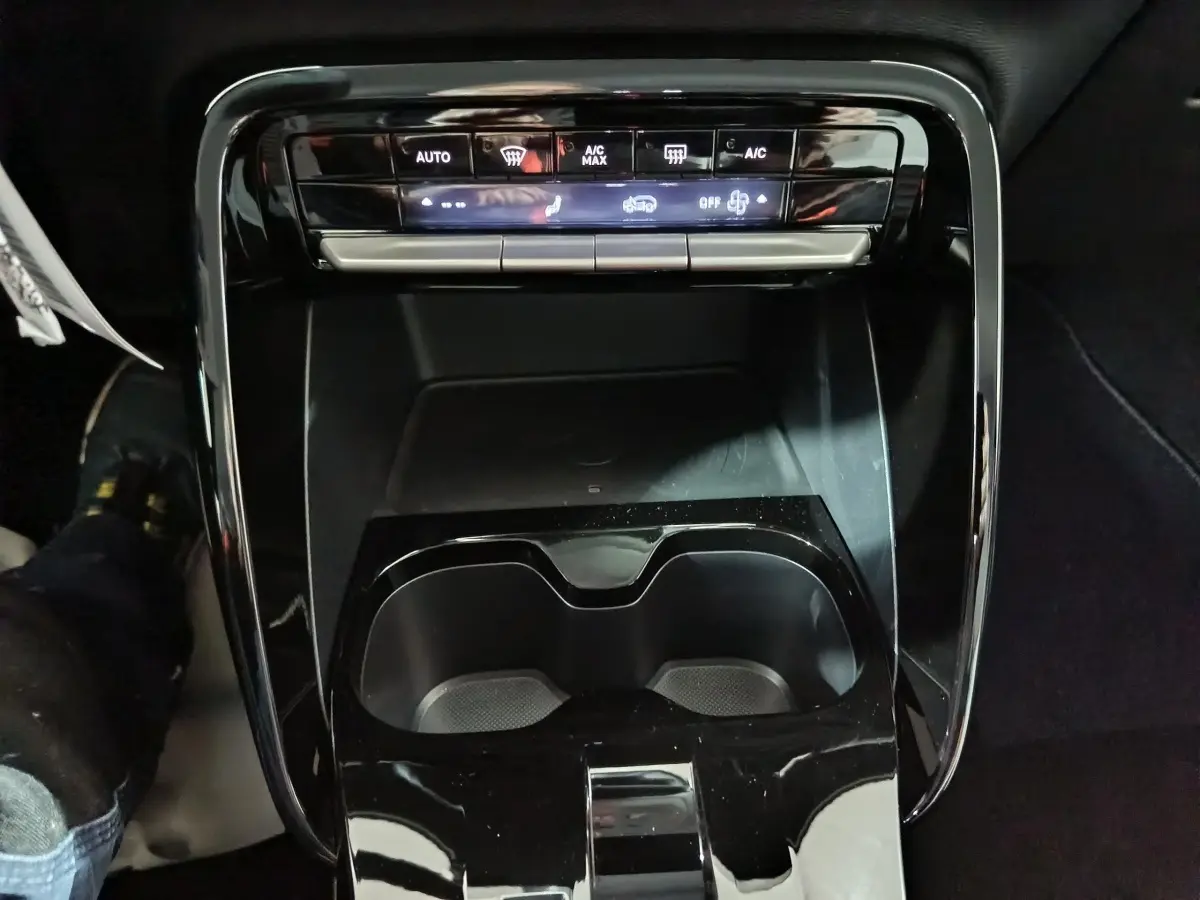 Vue rapprochée de la console centrale noire de la Citroën C3 hybride 2025, avec commandes climatisation et porte-gobelets.