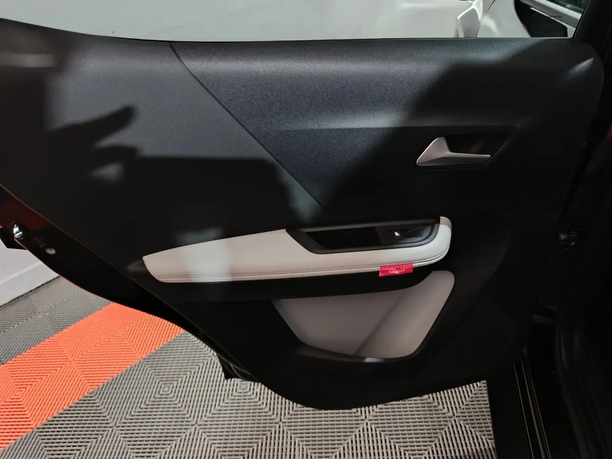 Vue intérieure côté gauche de la porte arrière noire de la Citroën C3 hybride avec accoudoir clair et poignée argentée.