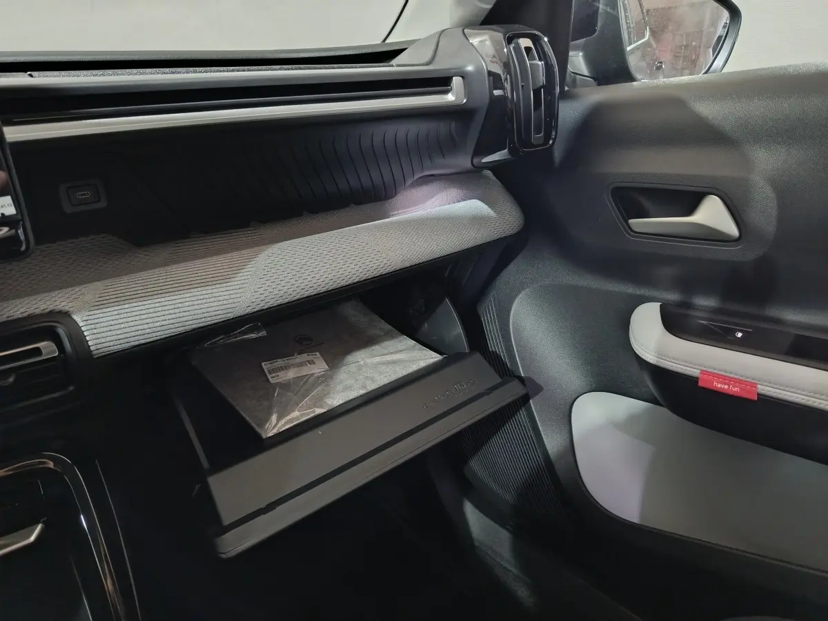 Intérieur de la Citroën C3 Hybride 2025, vue côté passager avec boîte à gants ouverte et garnitures grises et noires.