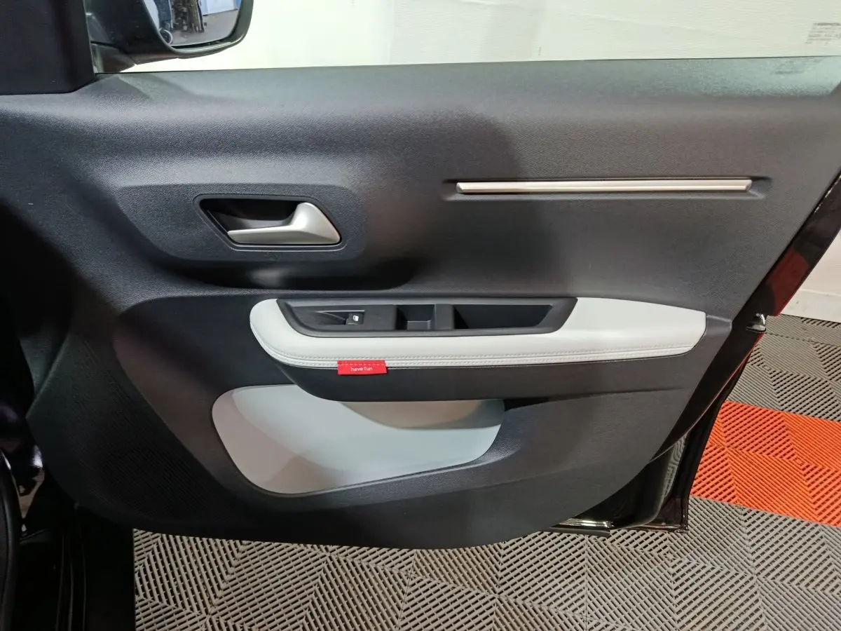 Vue intérieure du panneau de porte côté gauche de la Citroën C3 hybride noire, avec insert blanc et poignée argentée.