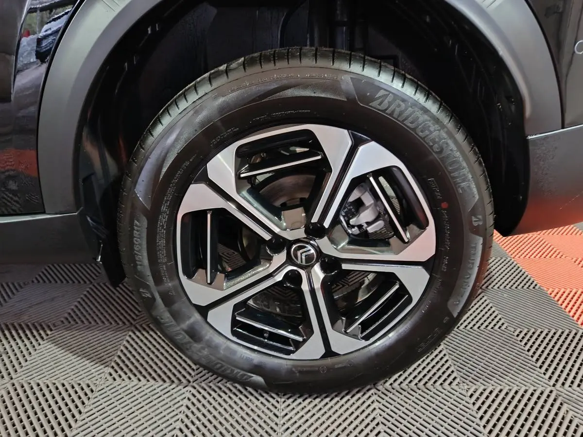 Gros plan sur la roue avant droite noire d'une Citroën C3 Hybride 136 e-DSC6 MAX avec jante alliage bicolore.