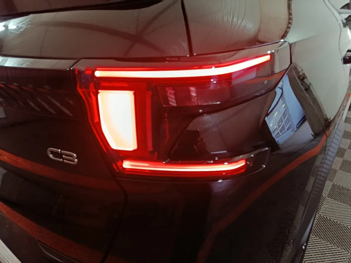 Feu arrière droit allumé d'une Citroën C3 noire, vue rapprochée sur le logo et les lignes lumineuses distinctives.