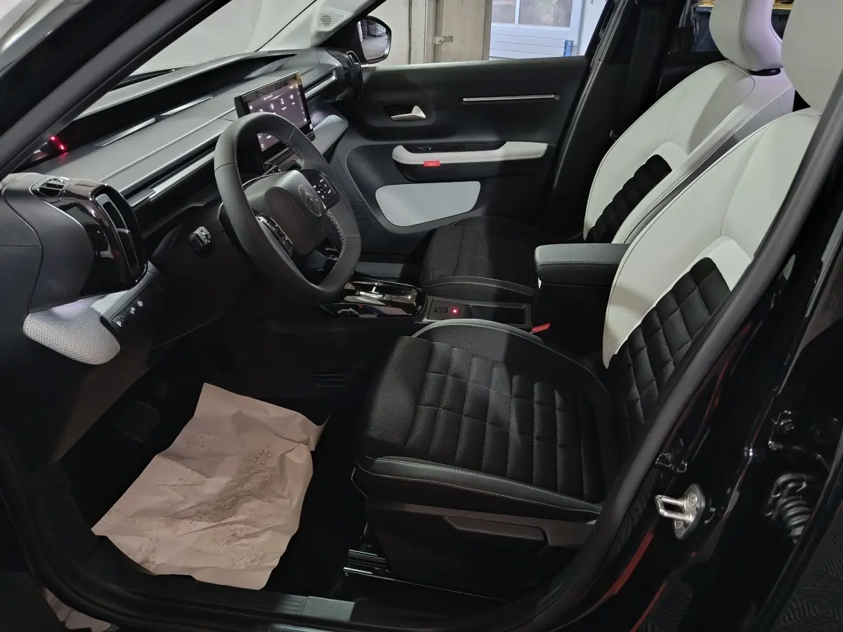 Vue intérieure côté conducteur de la Citroën C3 hybride 2025, sièges bicolores noir et blanc avec tableau de bord moderne.