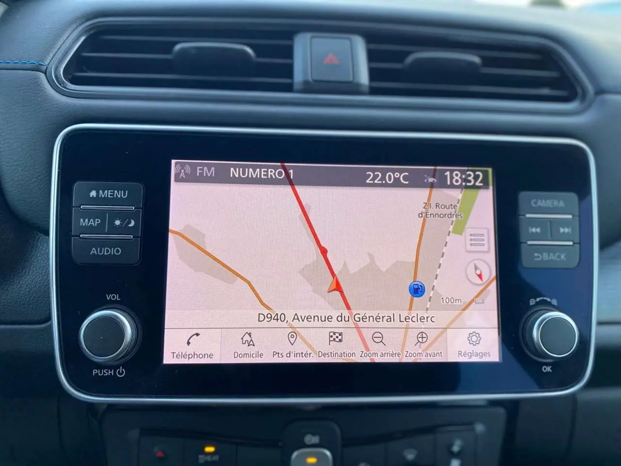 Gros plan sur l’écran tactile central du Nissan Leaf blanc 2020, affichant la navigation avec carte et commandes autour.