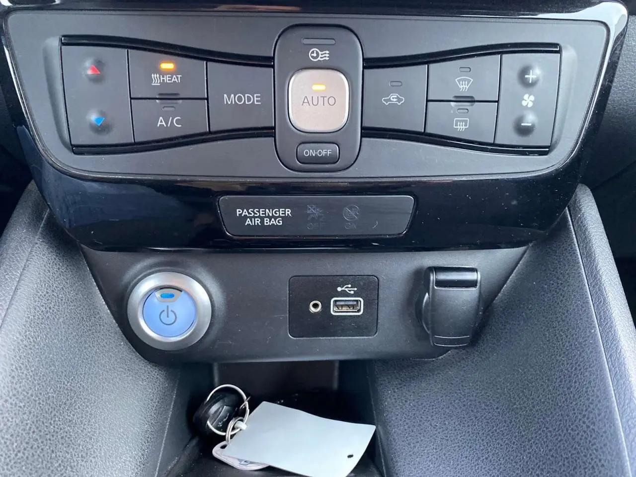 Détail de la console centrale du Nissan Leaf blanc 2020, montrant les commandes de climatisation et les ports USB et allume-cigare.