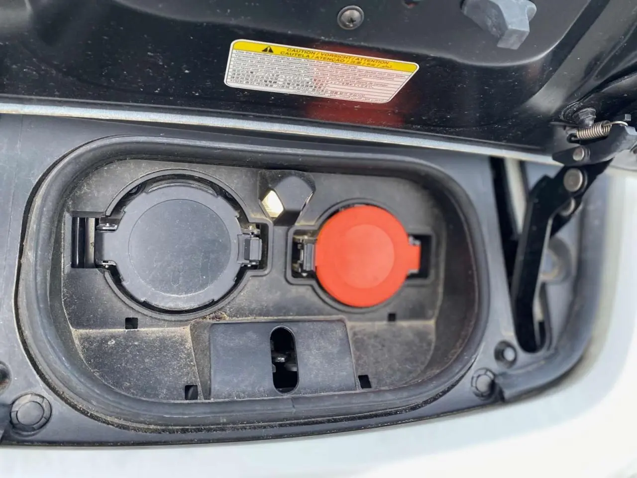 Prise de recharge électrique ouverte sur une Nissan Leaf blanche, vue rapprochée du compartiment de charge.