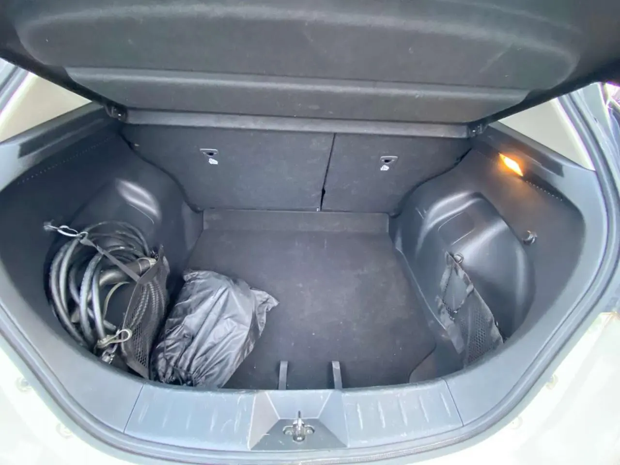 Coffre ouvert de Nissan Leaf blanche 2020, vue intérieure montrant un câble de recharge et un sac noir.