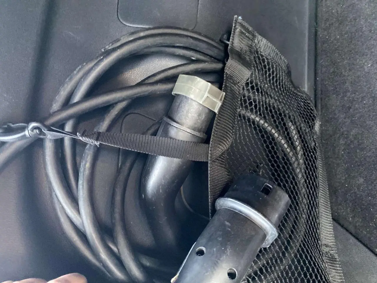 Gros plan sur le câble de recharge noir enroulé dans le coffre d'une Nissan Leaf blanche électrique.