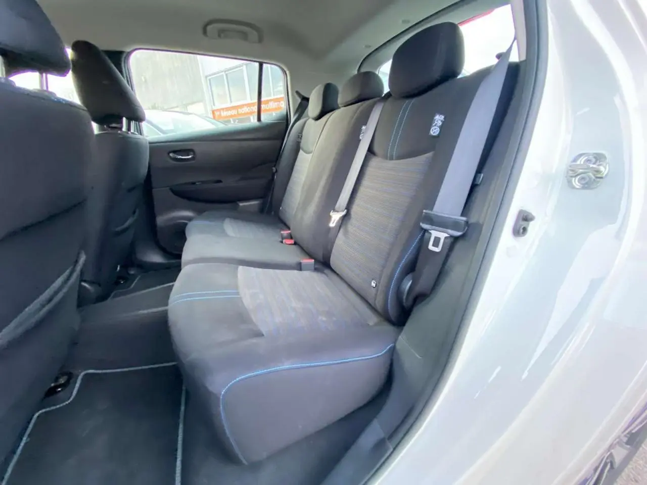 Vue intérieure arrière côté droit du Nissan Leaf blanc 2020, montrant les sièges arrière en tissu noir avec surpiqûres bleues.