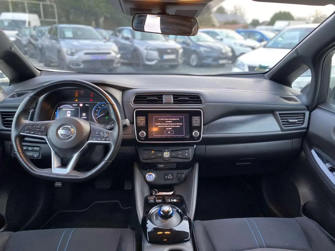 Vue intérieure avant du Nissan Leaf blanc 2020, tableau de bord avec écran tactile central et volant multifonction.