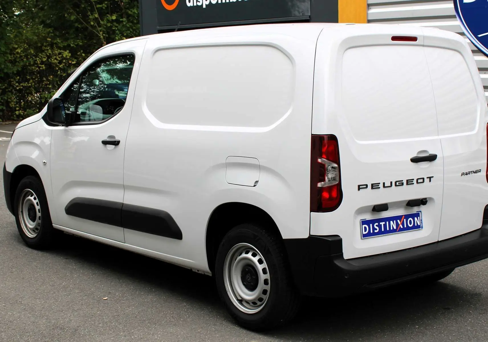 Vue 3/4 arrière droite du Peugeot Partner Fourgon blanc 2025 avec logo distinctif et porte latérale pleine.