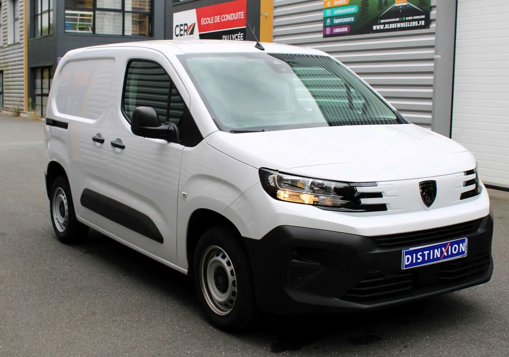Peugeot Partner Fourgon blanc vu en 3/4 avant droit, avec phares allumés et pare-chocs noir mat.