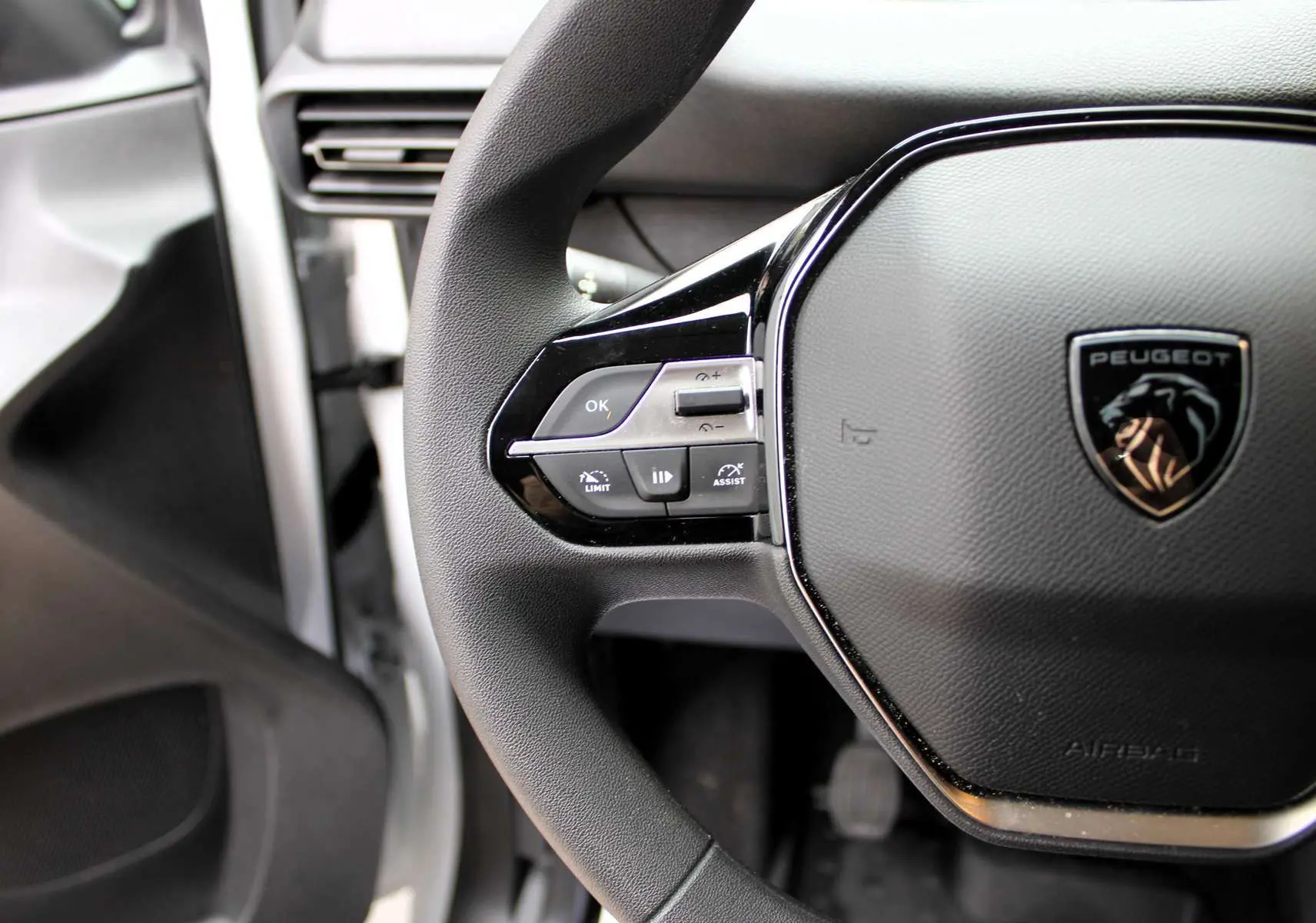 Gros plan sur le volant multifonction noir du Peugeot Partner Fourgon blanc 2025, avec logo lion et commandes intégrées.