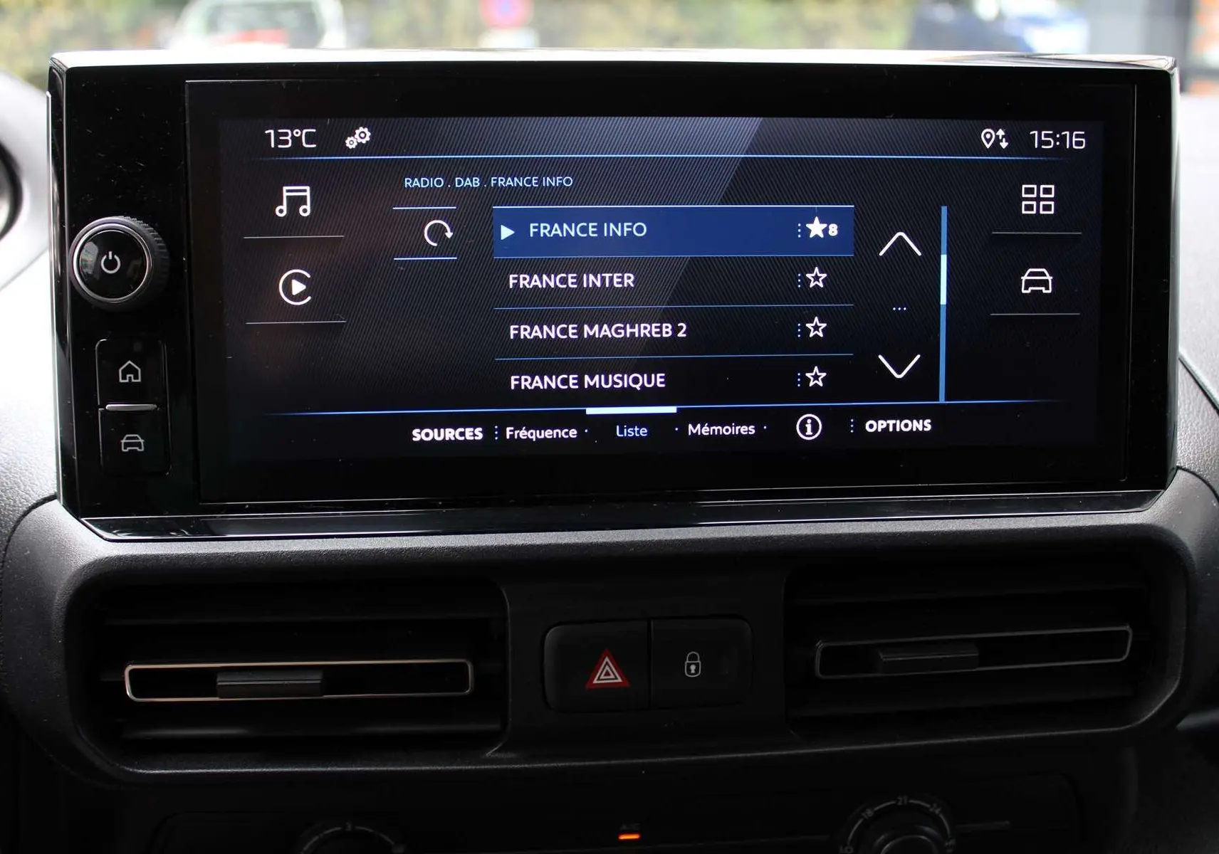 Écran tactile central du Peugeot Partner Fourgon 2025 affichant les stations radio, entouré de commandes et aérateurs noirs.