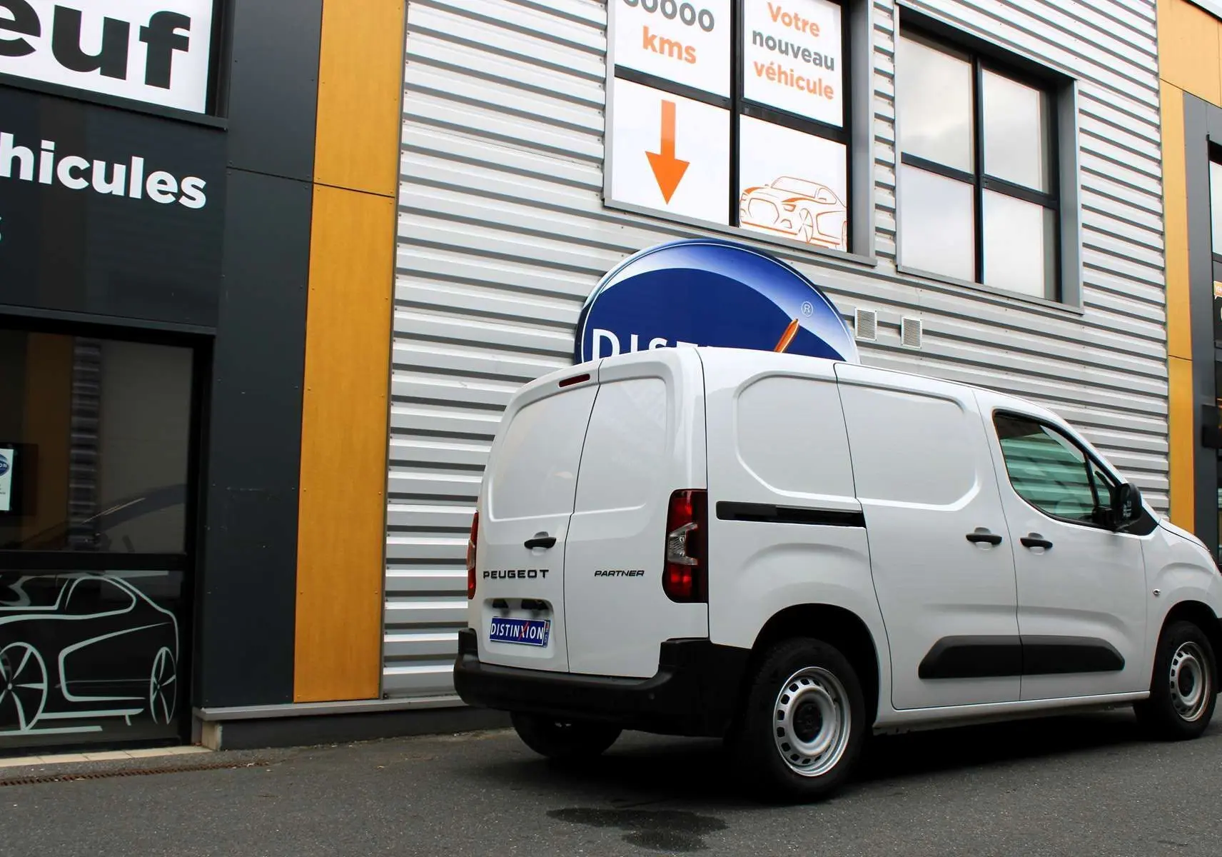 Vue 3/4 arrière droite d'un Peugeot Partner Fourgon blanc stationné devant un bâtiment commercial.