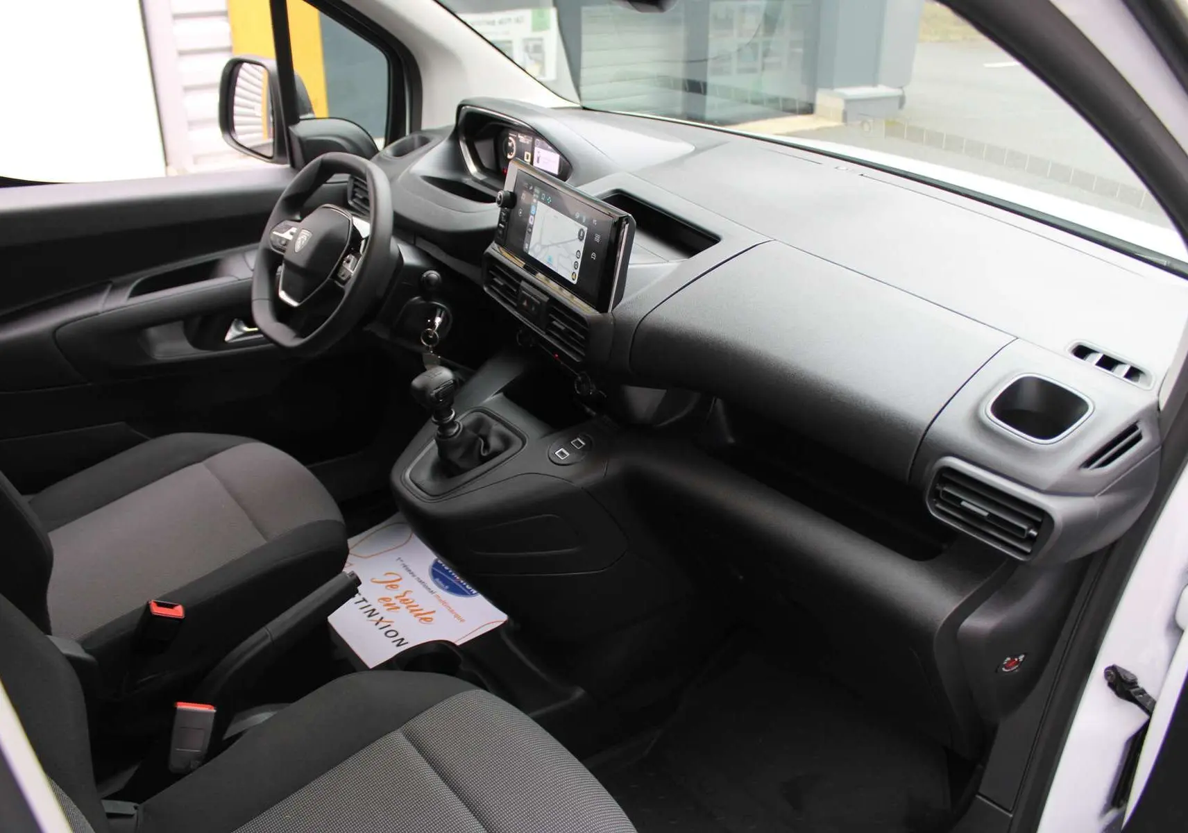 Intérieur du Peugeot Partner Fourgon 2025 vu côté conducteur, tableau de bord noir avec écran tactile et boîte manuelle.