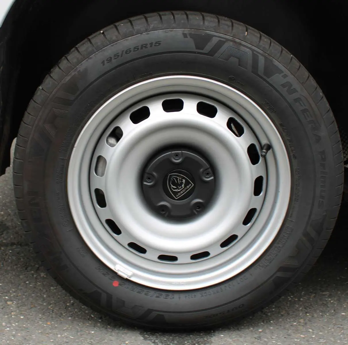 Gros plan sur la roue acier grise avec logo Peugeot du Partner Fourgon blanc, mettant en valeur le pneu et la jante simple.