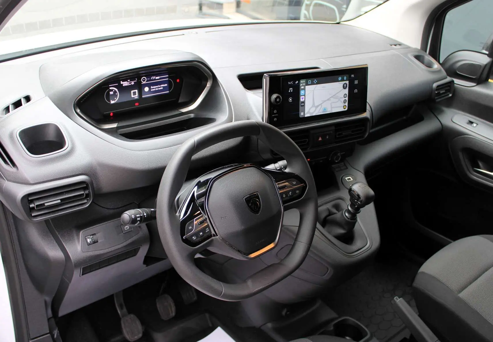 Intérieur du Peugeot Partner Fourgon 2025, vue du poste de conduite avec volant, écran tactile et levier de vitesse manuel.