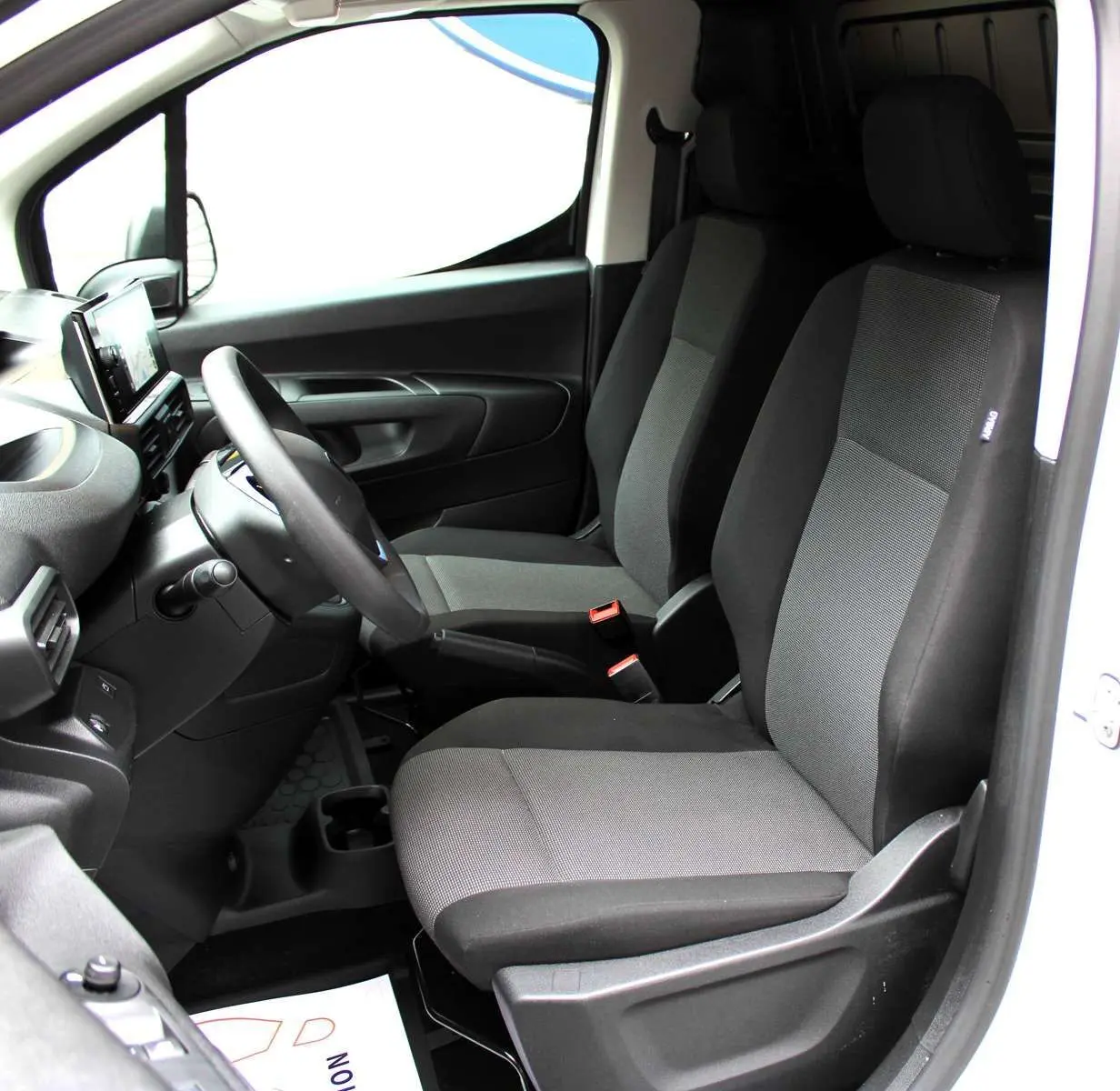 Vue intérieure côté conducteur du Peugeot Partner Fourgon 2025, sièges tissu gris et noir, tableau de bord moderne noir.