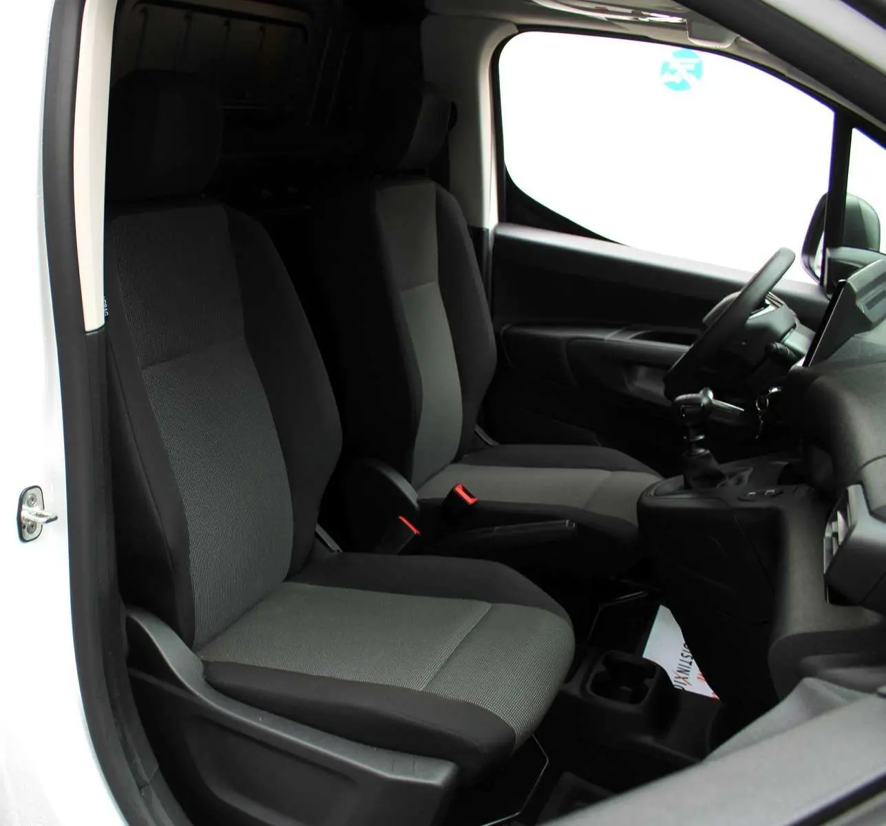 Vue intérieure côté conducteur du Peugeot Partner Fourgon blanc 2025, montrant les sièges avant et le volant.