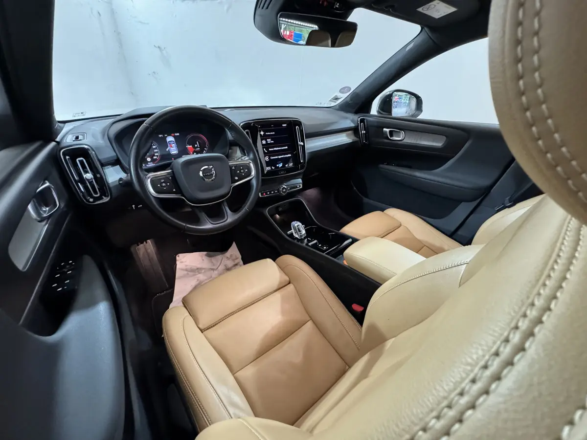 Vue intérieure avant du Volvo XC40 Recharge T5 2021, sièges cuir beige et tableau de bord noir avec écran tactile central.