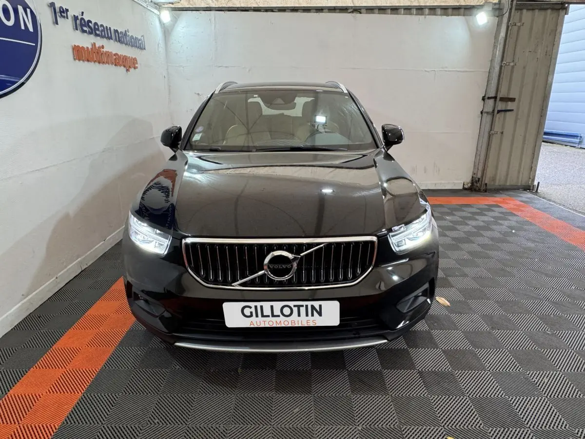 Vue frontale d'un Volvo XC40 noir hybride rechargeable avec phares LED allumés dans un showroom.