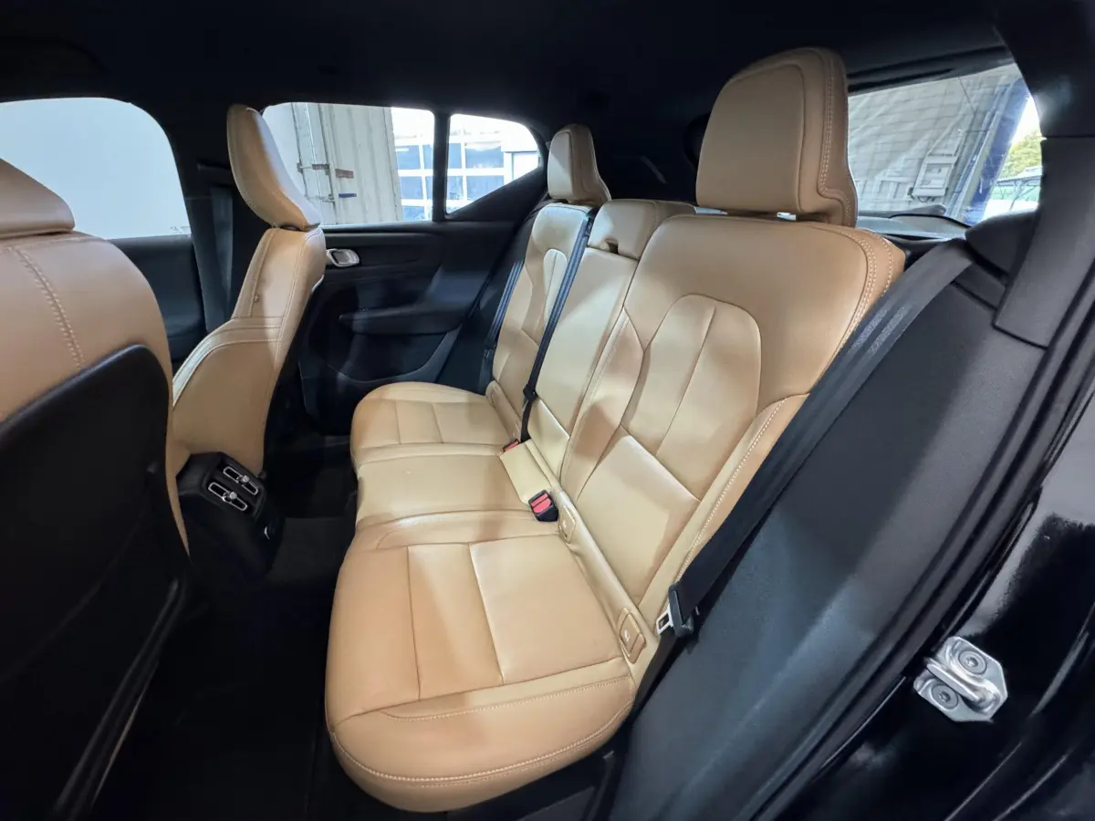 Vue intérieure côté droit des sièges arrière en cuir beige du Volvo XC40 noir, avec ceinture de sécurité et porte ouverte.