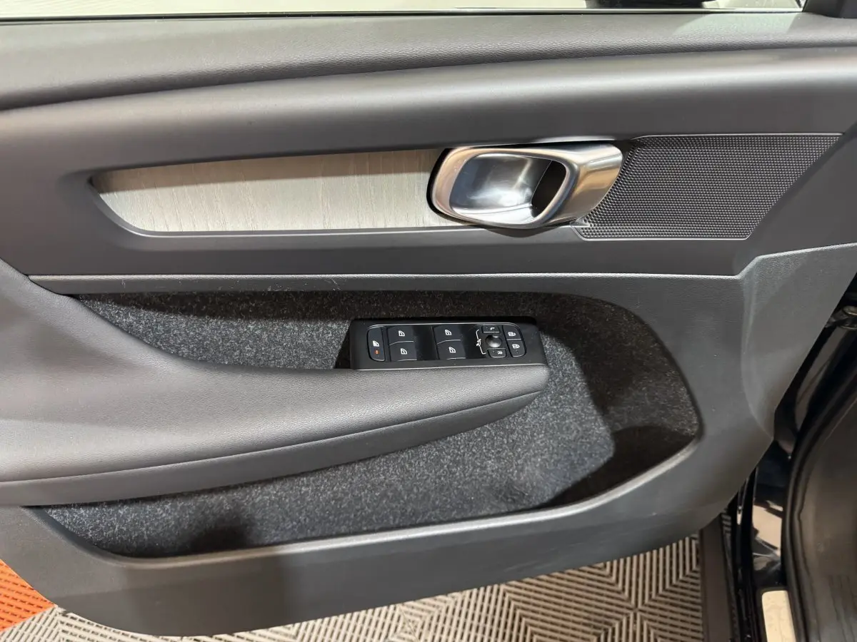 Gros plan sur la porte avant gauche noire du Volvo XC40 Recharge T5, avec commandes électriques et poignée alu.