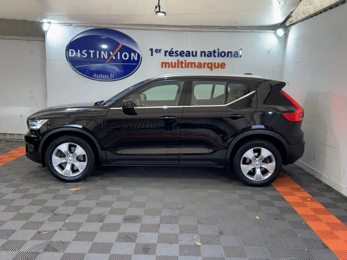 Profil côté gauche d'un Volvo XC40 Recharge T5 noir, hybride rechargeable, avec jantes argentées dans un garage.