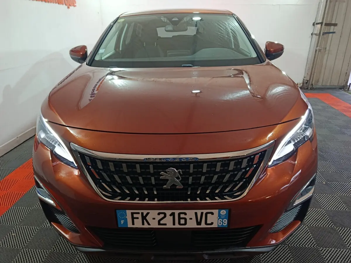 Vue frontale d'un Peugeot 3008 marron métallisé avec calandre chromée et phares LED allumés, en intérieur.