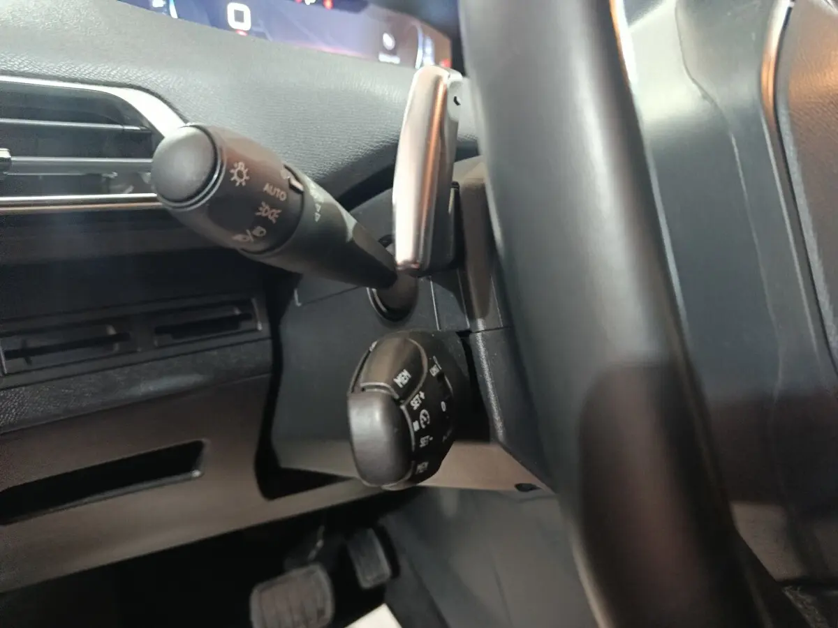 Gros plan sur la colonne de direction et commandes derrière le volant cuir noir d’un Peugeot 3008 marron, tableau de bord partiel visible.