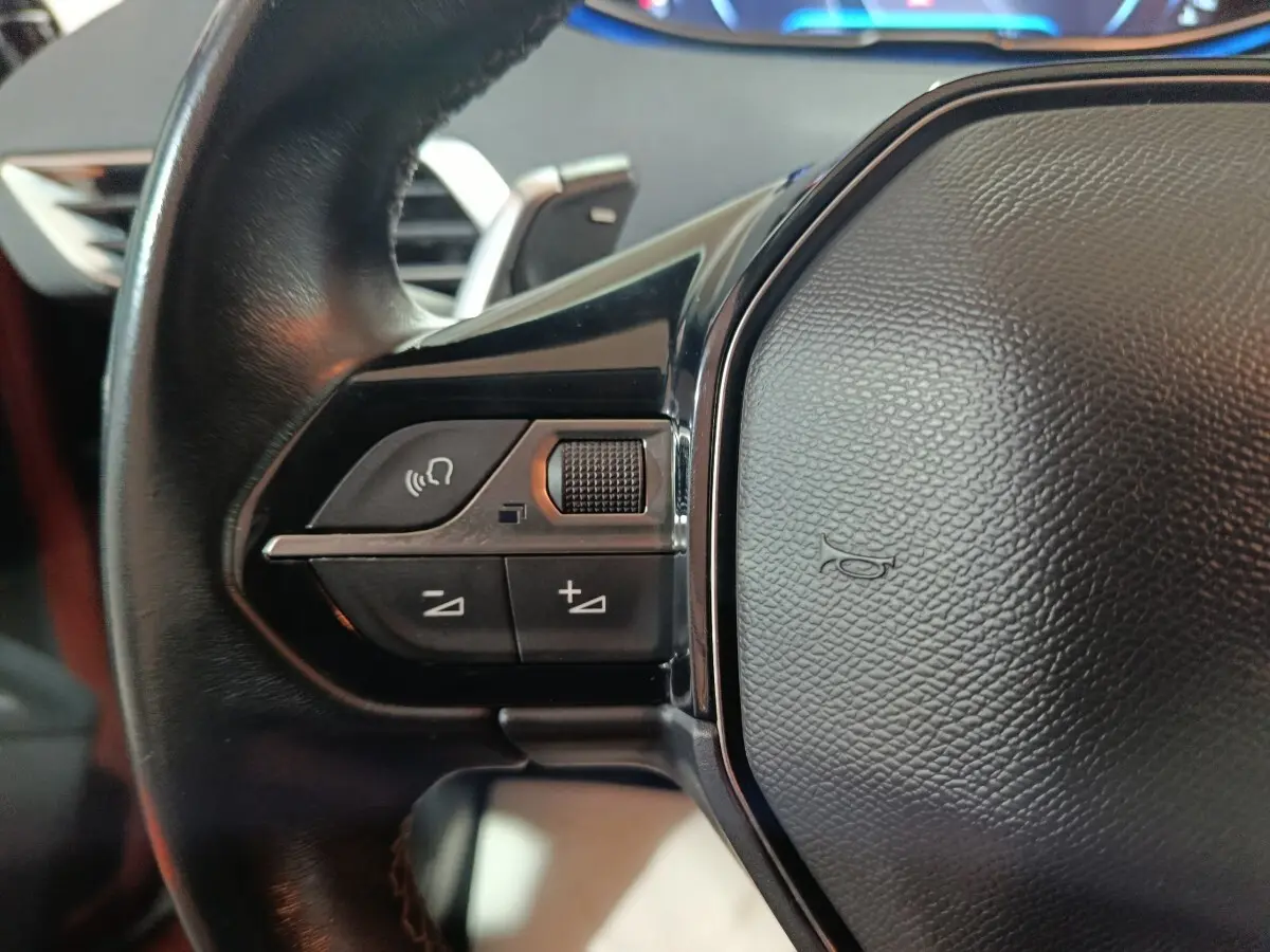 Gros plan sur le volant cuir noir du Peugeot 3008 2019, avec commandes audio et bouton klaxon visible.