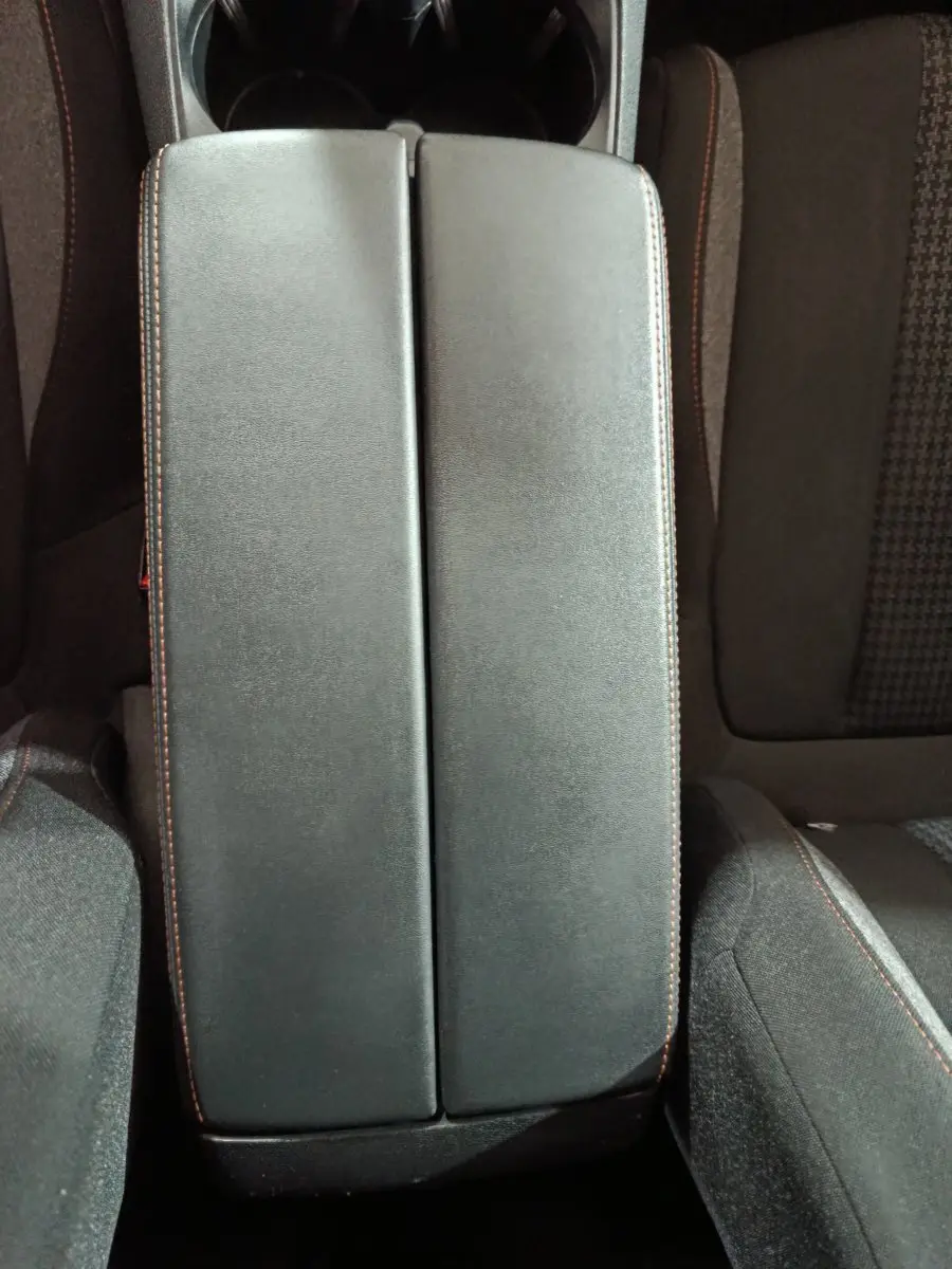 Vue plongeante sur l'accoudoir central noir avec surpiqûres marron entre les sièges avant du Peugeot 3008 marron.