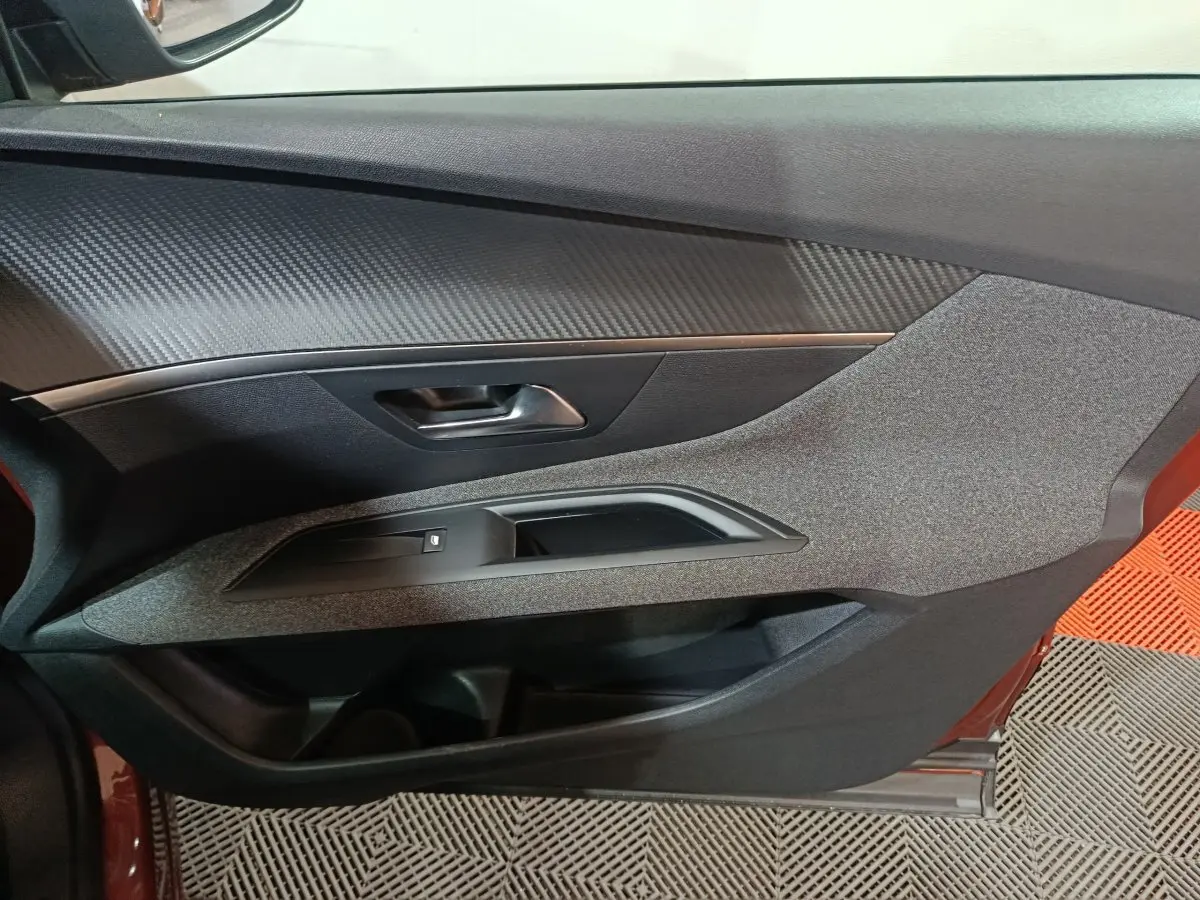 Vue intérieure du panneau de porte côté conducteur du Peugeot 3008 marron, avec insert imitation carbone et commande de vitre.