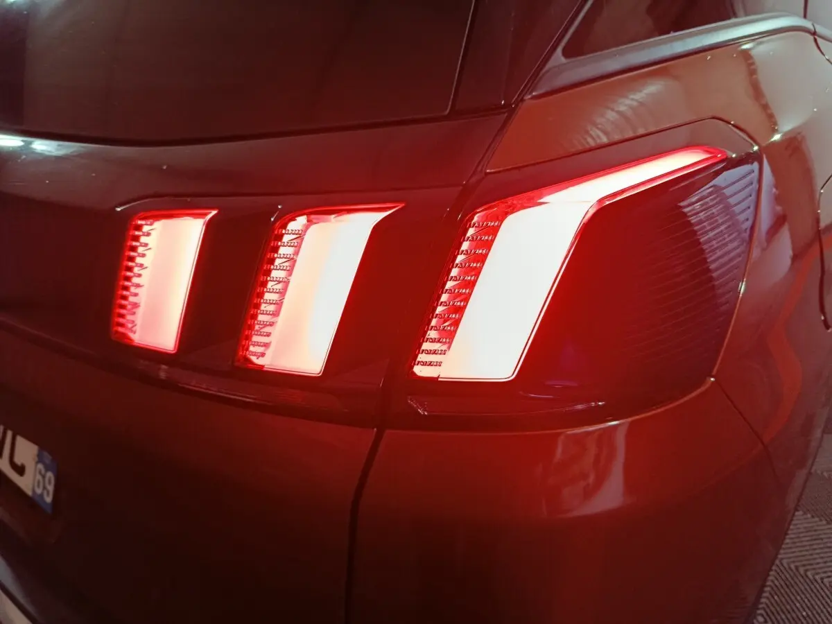 Gros plan sur le feu arrière droit rouge et blanc d’un Peugeot 3008 marron, vue arrière en faible lumière.