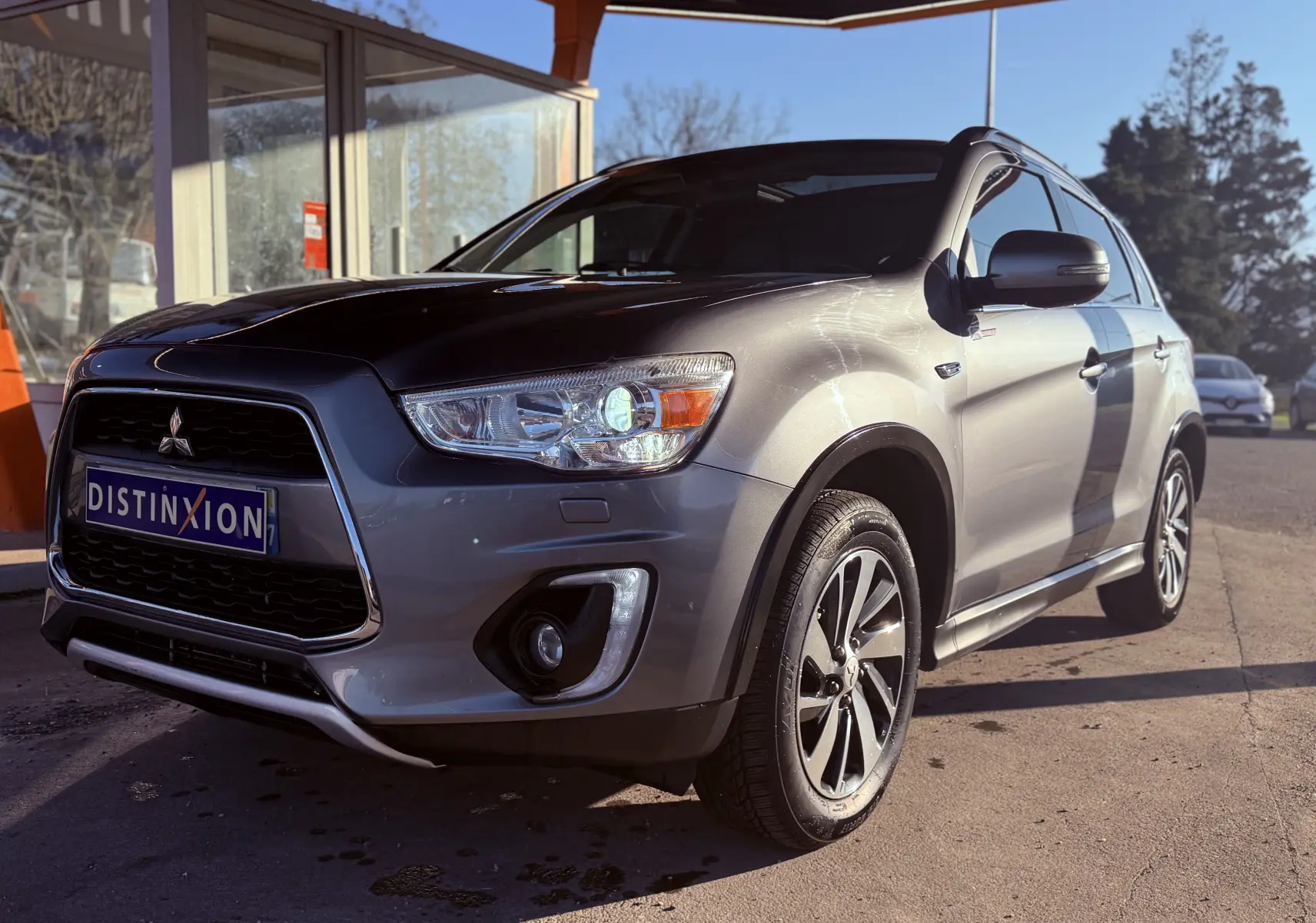 Vue 3/4 avant droit d’un Mitsubishi ASX gris métallisé garé sous un abri avec jantes alliage et calandre noire.