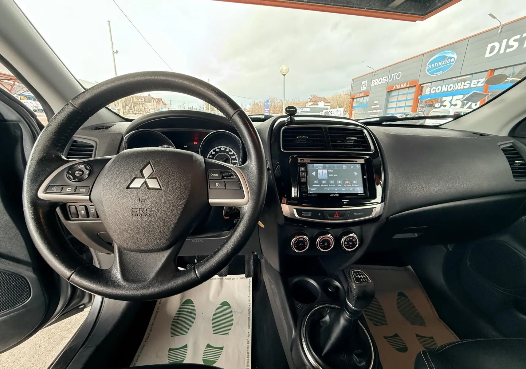Vue intérieure avant centrée sur le volant noir et la console centrale avec écran tactile du Mitsubishi ASX gris de 2015.