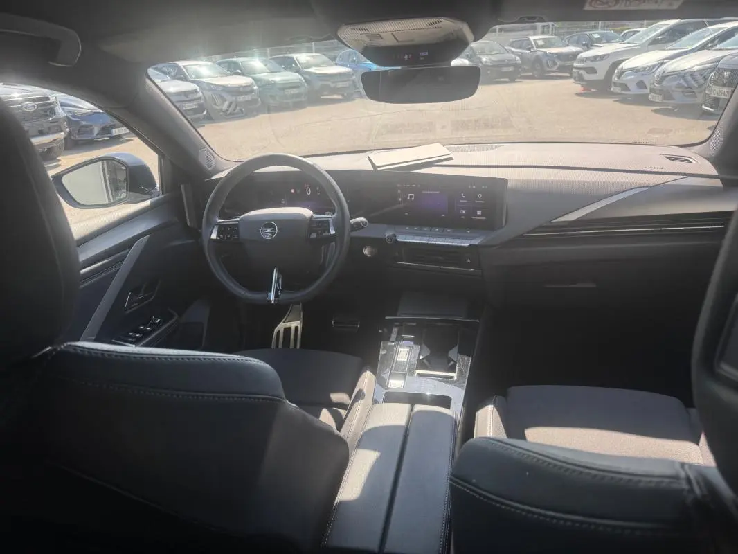 Vue intérieure avant de l’Opel Astra 2024 noire, montrant le volant cuir, l’écran tactile large et l’accoudoir central.