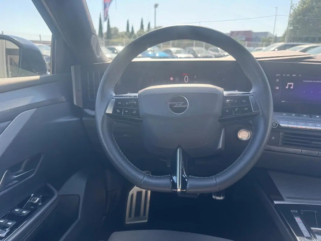 Vue intérieure centrée sur le volant cuir noir de l'Opel Astra 2024 avec commandes intégrées et tableau de bord digital.