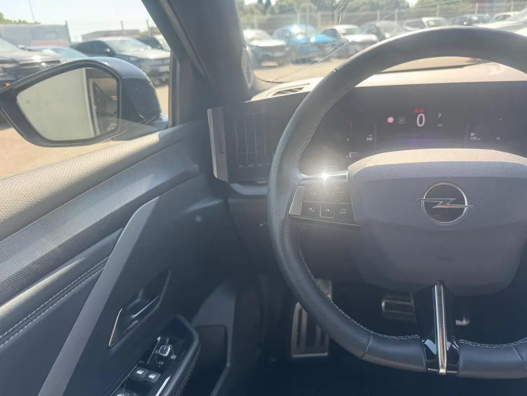Vue intérieure côté conducteur de l'Opel Astra 2024 noire, volant cuir avec commandes intégrées et rétroviseur électrique.
