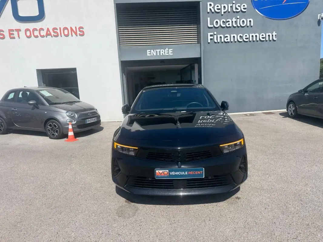 Vue frontale d'une Opel Astra noire 2024 avec feux LED allumés, stationnée devant un bâtiment commercial.