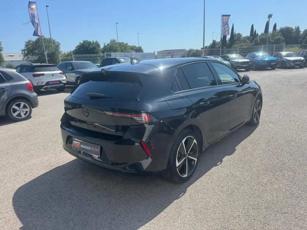 Opel Astra noir vue 3/4 arrière droit, vitres surteintées et jantes alliage 17 pouces visibles en extérieur.