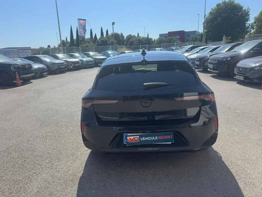 Vue arrière d'une Opel Astra noire 2024 avec vitres surteintées et feux arrière LED fins sur parking.