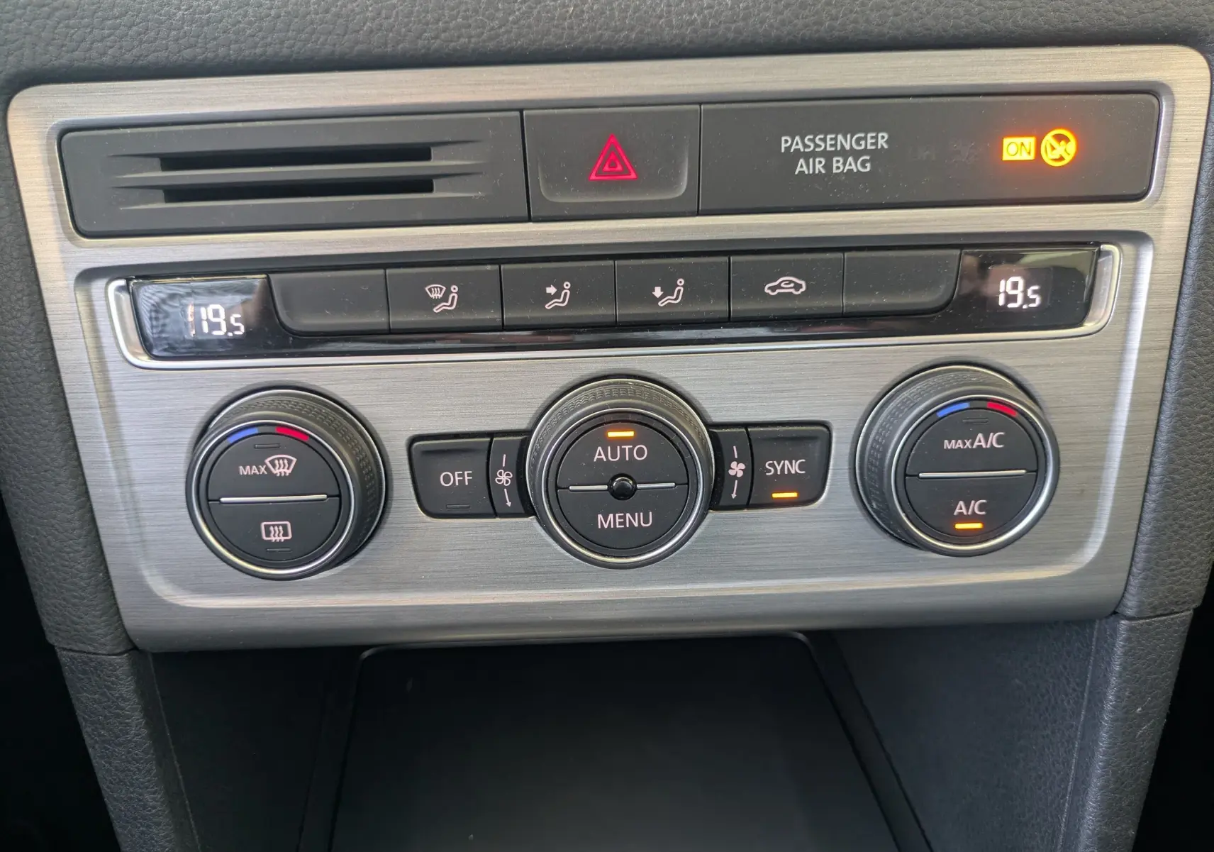 Vue rapprochée de la console centrale argentée du Volkswagen Golf Sportsvan noir, avec commandes de climatisation digitales.