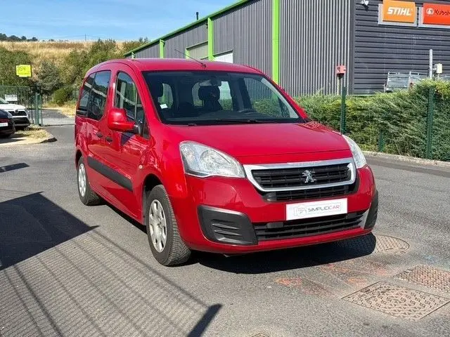 Vue 3/4 avant d’un Peugeot Partner Tepee rouge garé, mettant en valeur sa calandre noire et ses protections latérales noires.