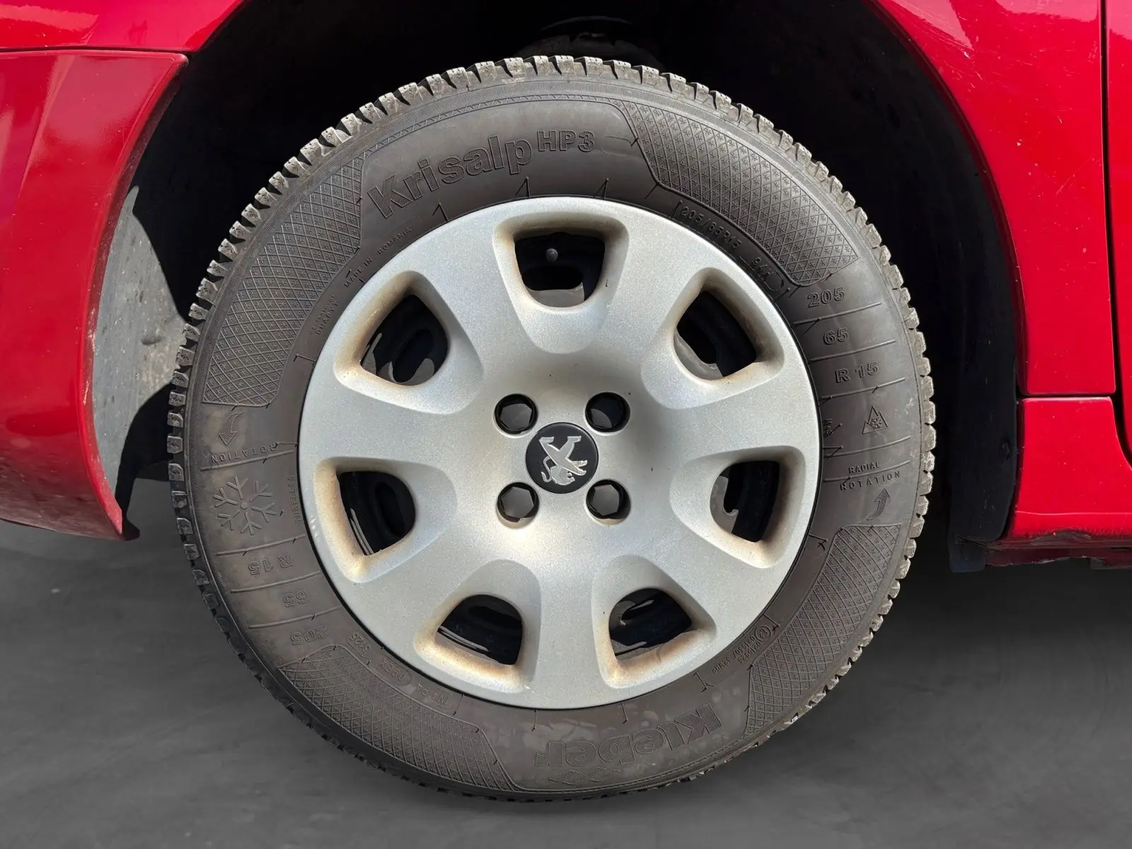 Gros plan sur la roue arrière droite d’un Peugeot Partner Tepee rouge de 2016, montrant le passage de roue et la carrosserie.