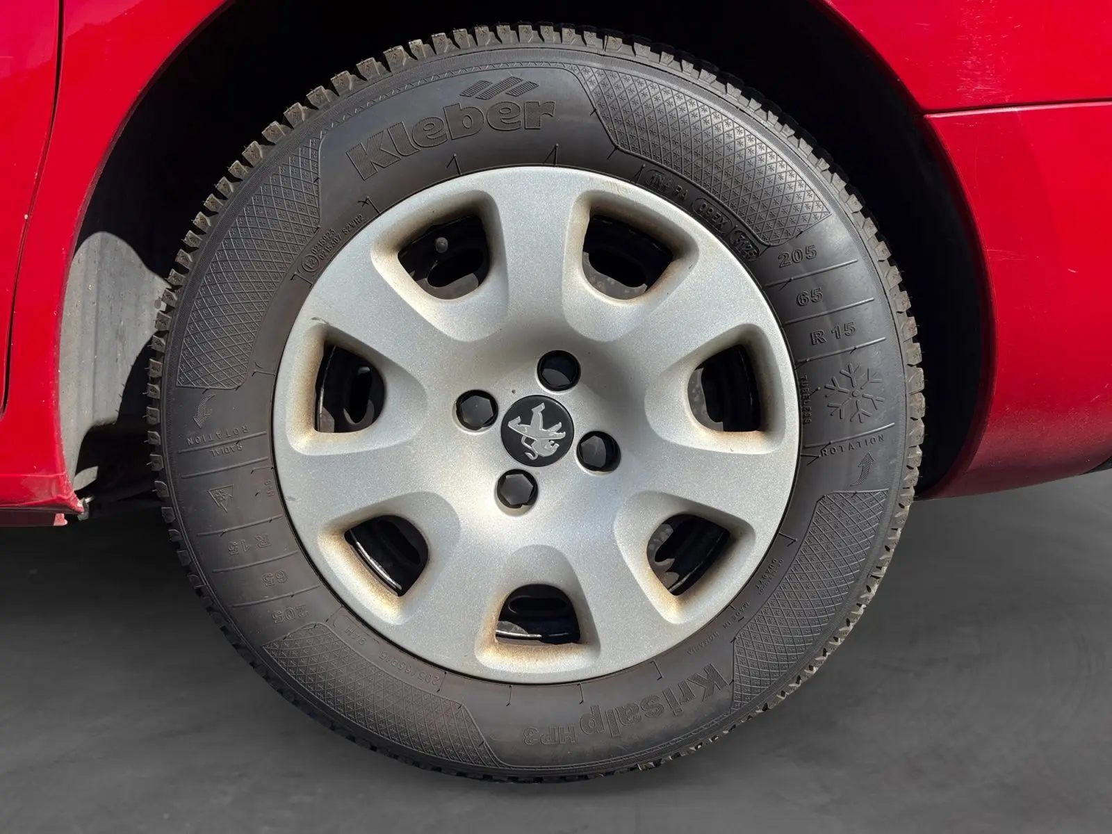 Gros plan sur la roue arrière droite d’un Peugeot Partner Tepee rouge de 2016, mettant en valeur la carrosserie et le pneu.