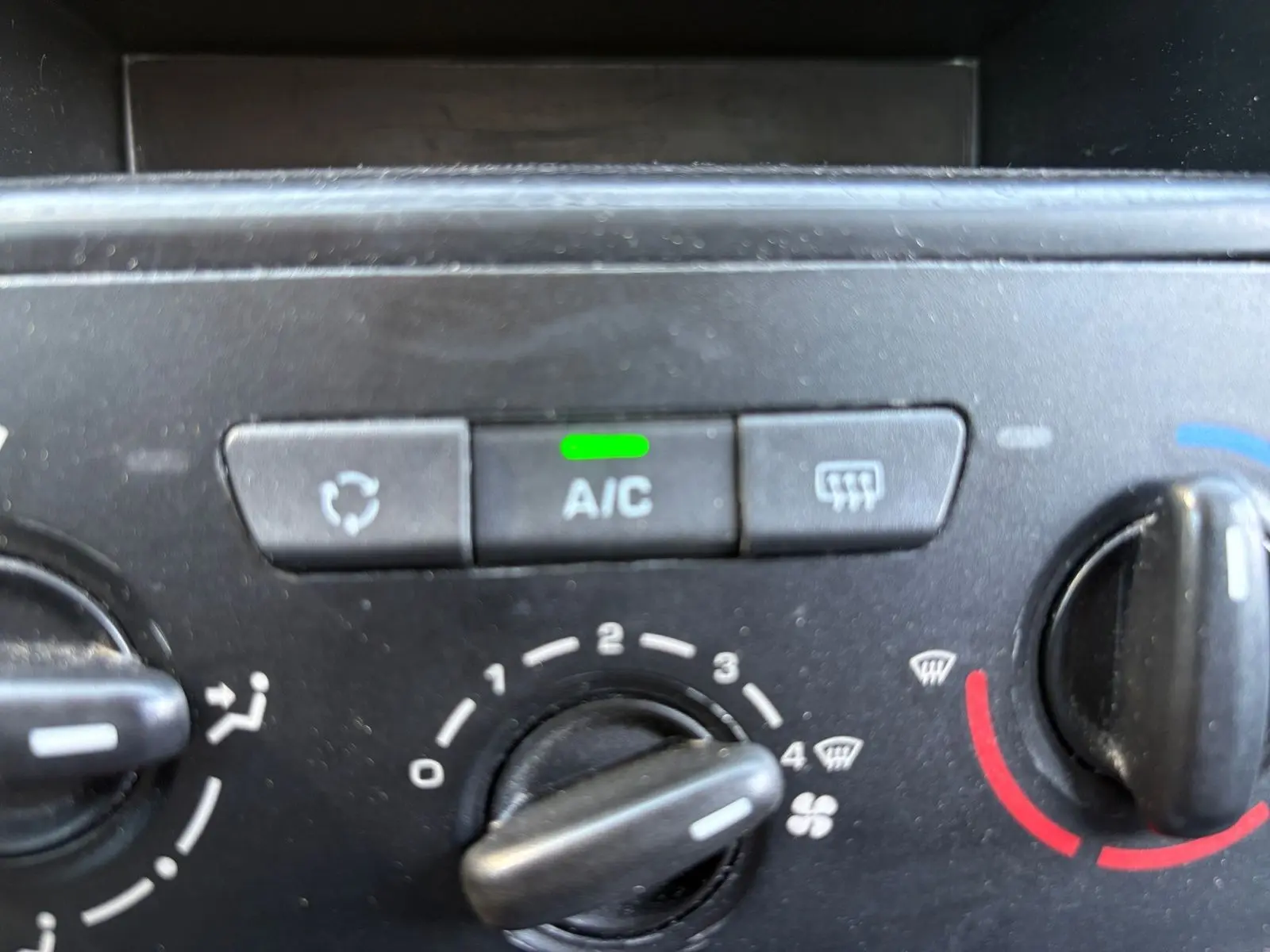 Gros plan sur le tableau de bord du Peugeot Partner Tepee rouge, mettant en valeur la commande de climatisation manuelle avec bouton A/C allumé.